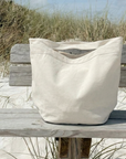 Beige tote bag on a wooden bench in a sandy area with grass
