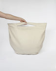 Beige cotton beach tote bag held by a hand on a white background
