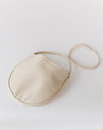 A natural, undyed leather shoulder bag rests on a white background. The leather is soft and the bag is a half moon shape.