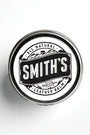 A metal tin of Smith's Leather Balm rests against a white backdrop. It features the company's black logo on a white sticker, with the words "all natural leather balm" and "made in Maine" underneath the company's name.