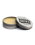 An open metal tin of Smith's Leather Balm rests against a white backdrop. It features the company's black logo on a white sticker, with the words "all natural leather balm" and "made in Maine" underneath the company's name.