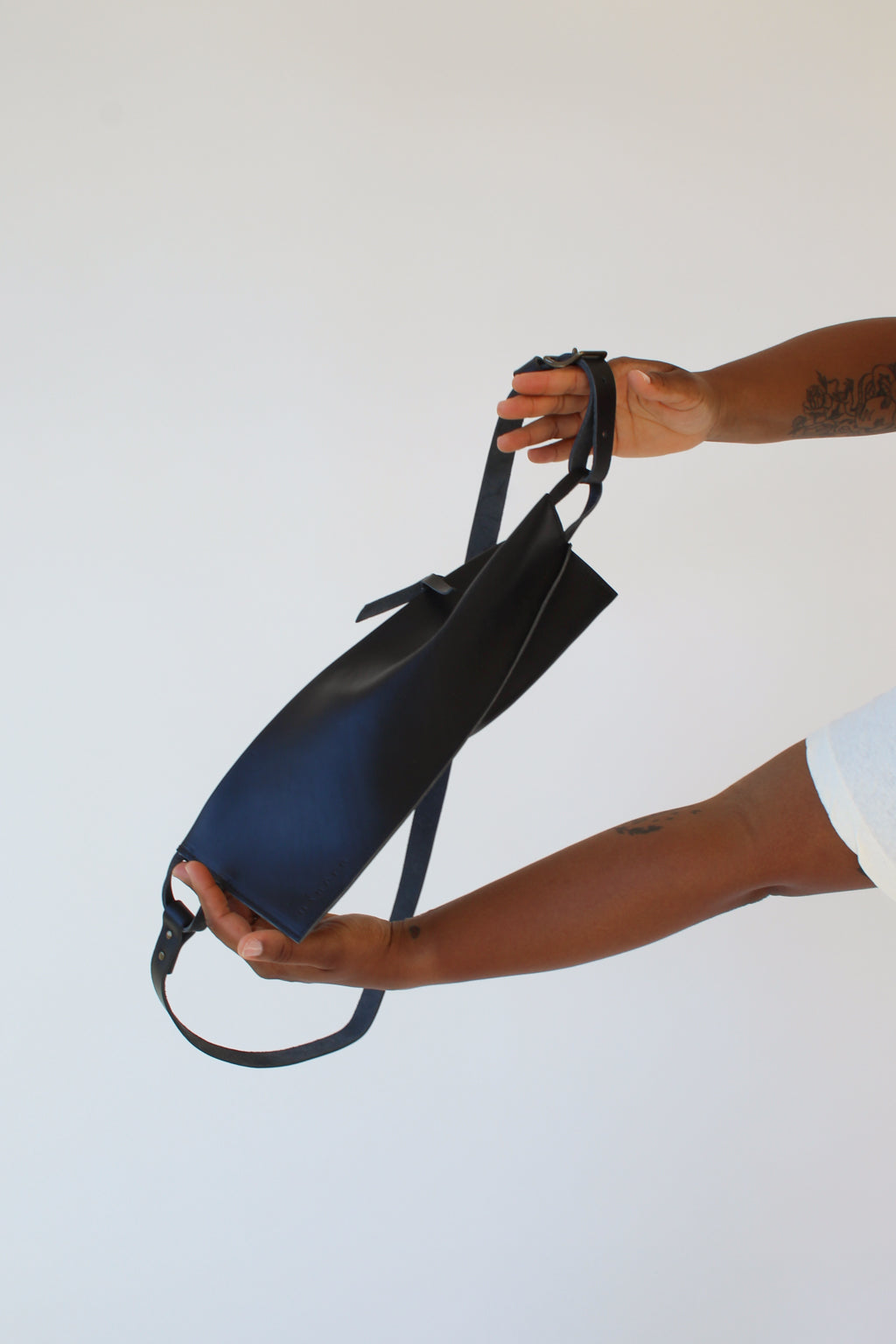 A woman holds out a black leather fanny pack shoulder bag against a white background.