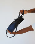 A woman holds out a black leather fanny pack shoulder bag against a white background.