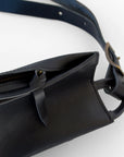 A close up of the zipper and zipper pull of a black leather fanny pack shoulder bag against a white background.