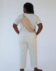 A woman wears a natural, undyed leather fanny pack shoulder bag against a white background. Her back faces the camera and the bag rests against her back.