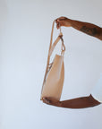 A woman holds out a natural, undyed leather fanny pack shoulder bag against a white background.
