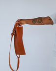 A woman holds out a light brown chestnut leather fanny pack shoulder bag against a white background.