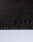 A detail of a black leather cardholder against a white background. The stitching is visible, as is the "Harper" logo.
