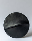 A circular black leather clutch rests against a white background.