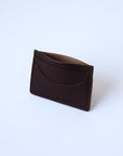 A dark brown leather cardholder sits against a white background. The stitching is visible, as is the "Harper" logo. The cardholder is propped slightly open, and is positioned at an angle.