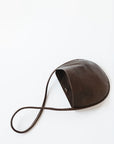 A dark brown leather shoulder bag rests on a white background. The leather is soft and shiny, and the bag is a half moon shape.