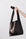 A woman's arm is visible, holding out the strap of a large, soft dark brown leather shoulder bag.