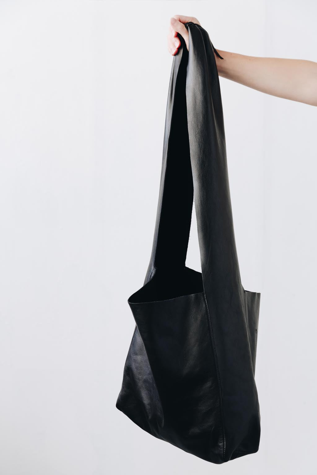 A woman's arm is visible, holding out the strap of a large, soft black leather shoulder bag.