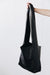 A woman's arm is visible, holding out the strap of a large, soft black leather shoulder bag.