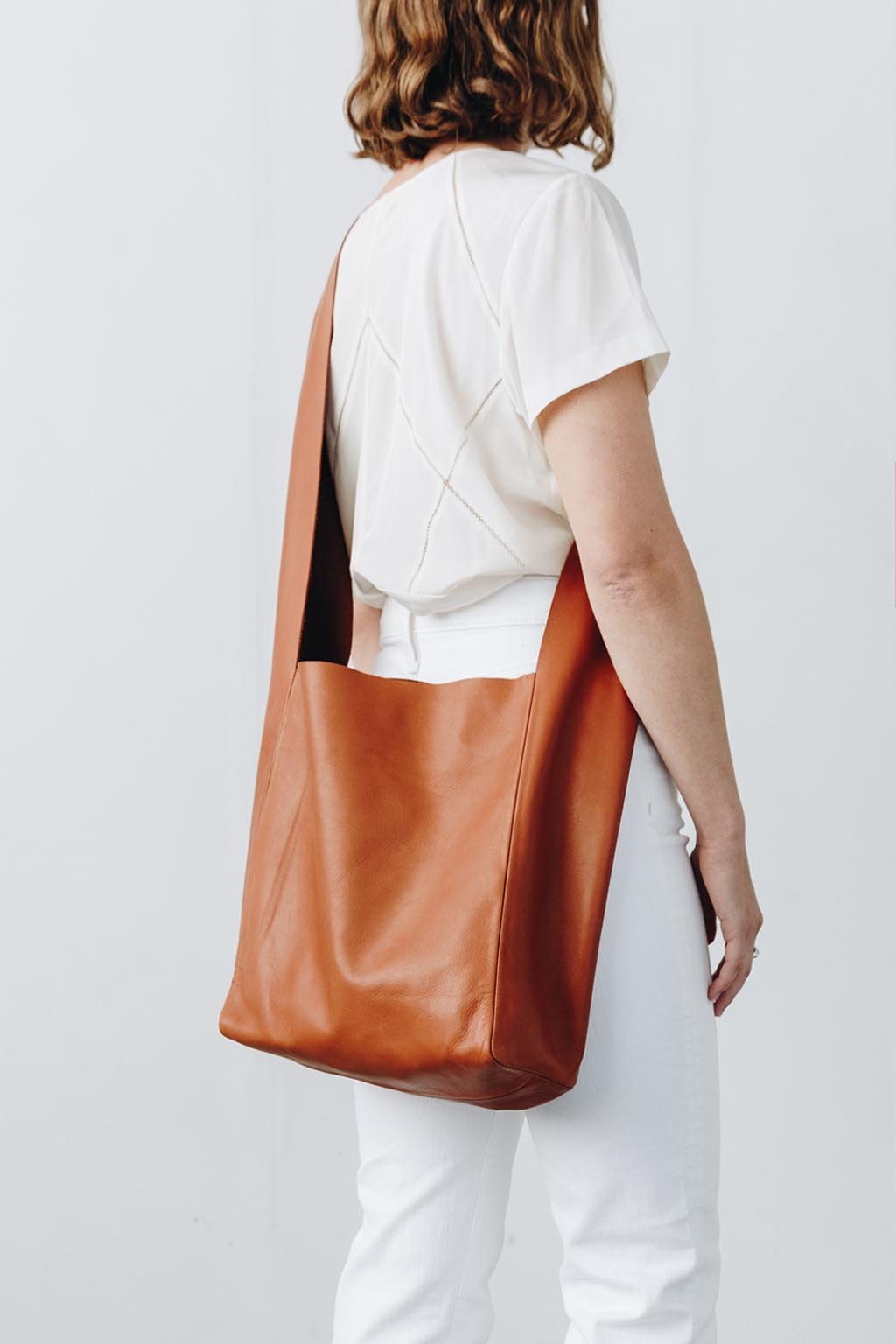 A woman wears a large, soft cognac brown leather shoulder bag across her body.