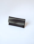 A black leather envelope wallet sits against a white background. It has the "Harper" logo heat stamped at the bottom, with the top flap secured by a brass button stud.