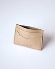A natural, undyed leather cardholder sits against a white background. The cardholder is propped open and shown at a slight angle. The stitching is visible, as is the "Harper" logo.