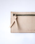 A natural, undyed leather envelope wallet sits against a white background. This close up shows the zipper at the reverse of the inner compartment, with a matching leather pull and the Harper logo heat stamped at the bottom.