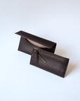 A dark brown leather envelope wallet sits against a white background. It has the "Harper" logo heat stamped at the bottom, with the top flap secured by a brass button stud. The inner component is in front of the outer one, showing a zipper and matching leather pull.