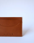 A detail of a light brown leather cardholder sits against a white background. The stitching is visible, as is the "Harper" logo.