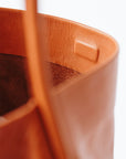 A detail of a cognac leather shoulder bag's magnetic closure, showing the interior of the bag.