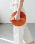 A woman holds a circular cognac brown leather clutch in her hands as she walks.