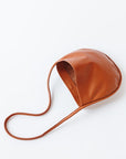A light brown, cognac leather shoulder bag rests on a white background. The leather is soft and shiny, and the bag is a half moon shape.