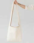 A woman's arm is visible, holding out the strap of a large, soft undyed, natural leather shoulder bag.