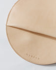 A circular natural, undyed leather clutch rests against a white background. The photo focused on the stitch and the embossed "Harper" logo.