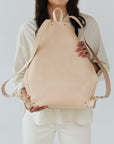 A woman holds out a natural, undyed leather backpack to show its reverse side.