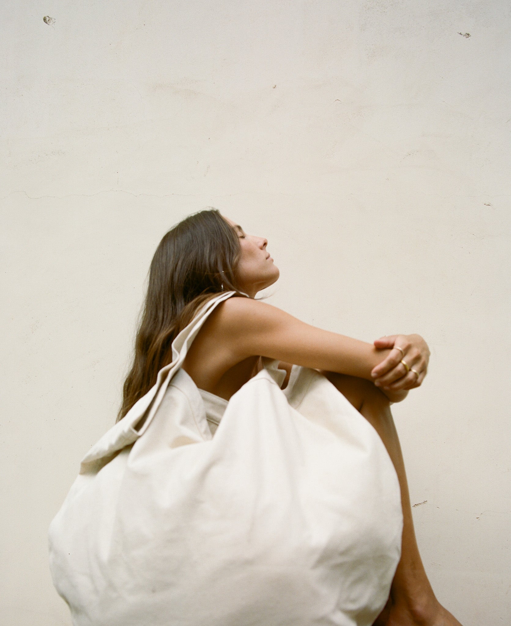 Woman sitting with a white bag on a plain background