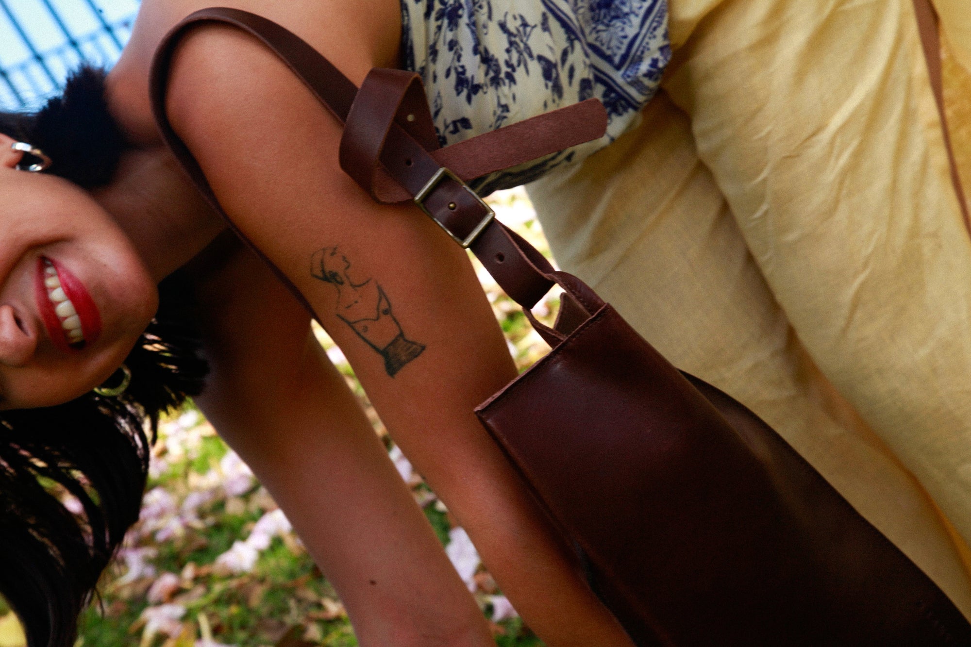 Woman with a tattoo on her arm, wearing a brown bag and yellow pants, outdoors.