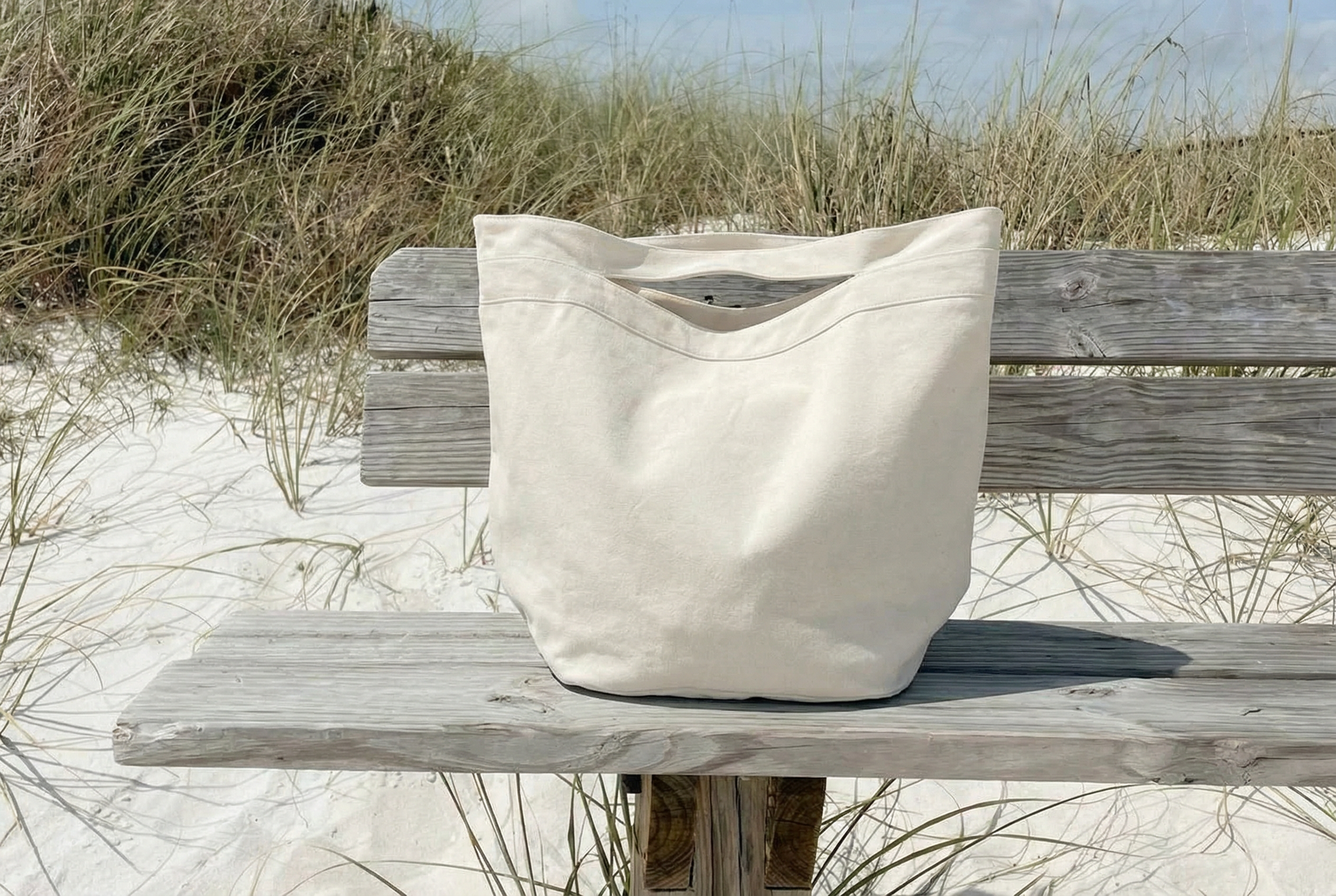 Beige tote bag on a wooden bench in a sandy area with grass