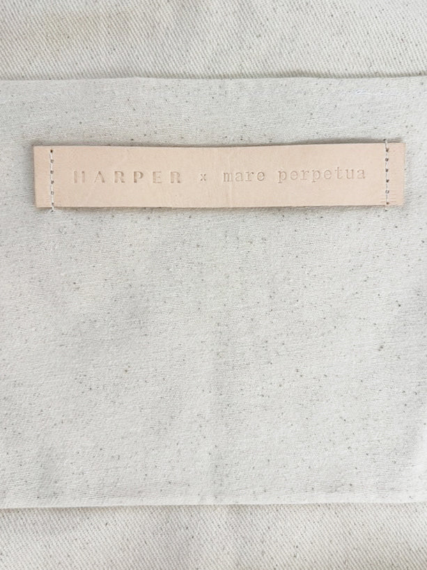 Close-up of a leather label with HARPER X MARE PERPETUA text on a textured gray fabric background