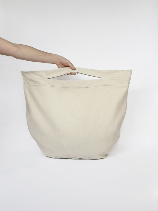 Beige cotton beach tote bag held by a hand on a white background