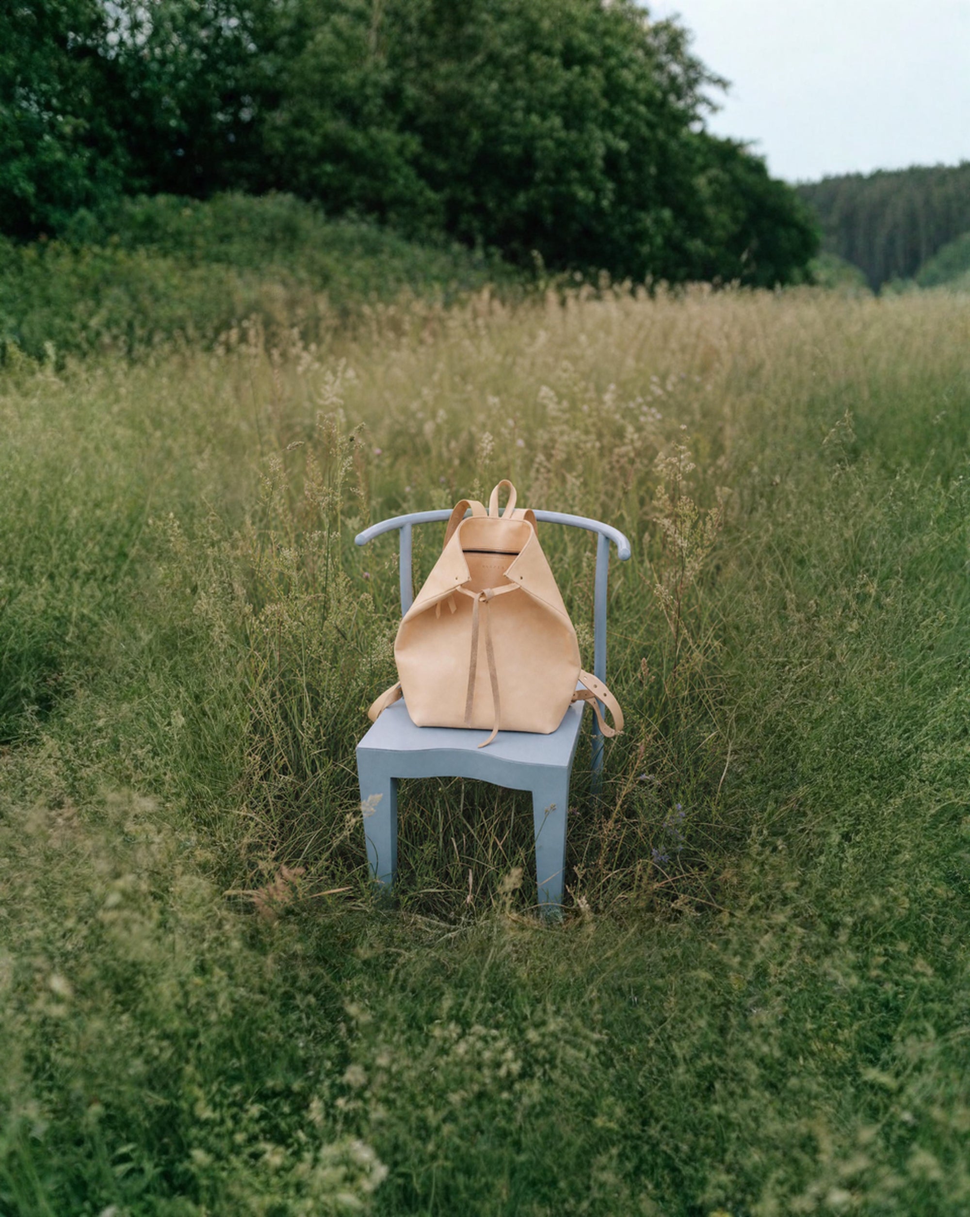 Beige backpack on a blue chair in a grassy field with trees in the background