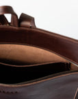 A detail of a dark brown leather backpack showing the top strap, zipper, and interior pocket of the backpack.