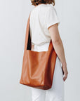 A woman wears a large, soft cognac brown leather shoulder bag across her body.